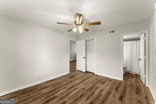 unfurnished bedroom featuring ensuite bath, ceiling fan, dark wood-type flooring, and a closet