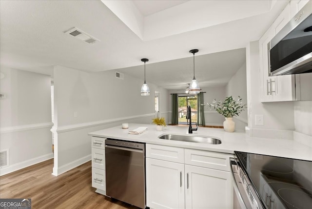 kitchen with appliances with stainless steel finishes, decorative light fixtures, white cabinets, light hardwood / wood-style flooring, and sink