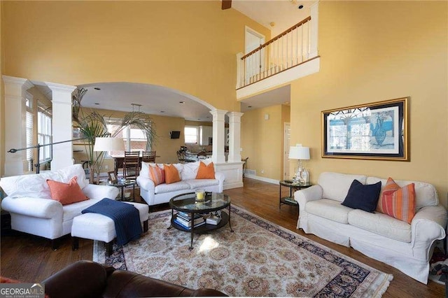 living room featuring dark wood-type flooring, a high ceiling, and decorative columns