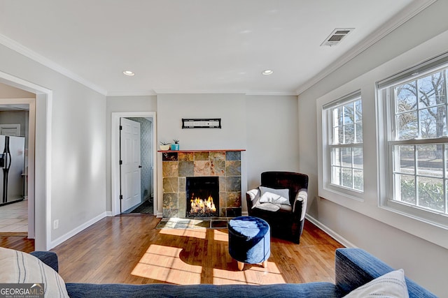 living room with plenty of natural light, wood-type flooring, crown molding, and a tiled fireplace