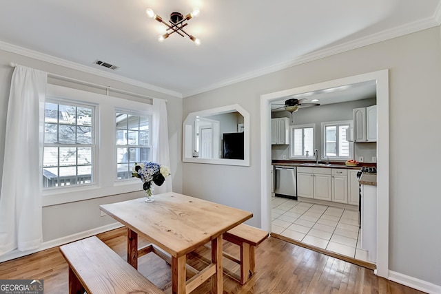 dining room featuring sink, light wood-type flooring, a healthy amount of sunlight, and crown molding