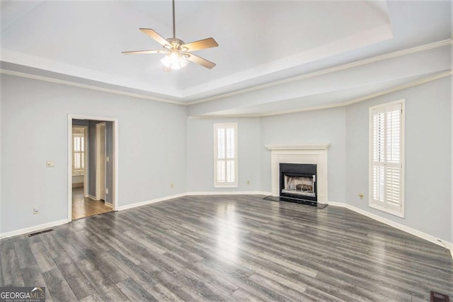 unfurnished living room featuring a raised ceiling, ceiling fan, dark wood-type flooring, and crown molding