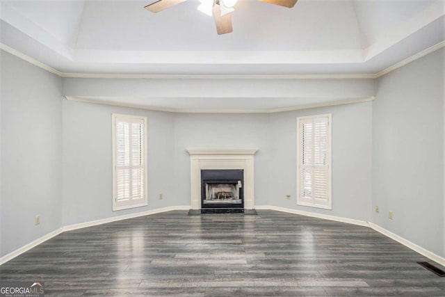 unfurnished living room with ceiling fan, a wealth of natural light, a tray ceiling, and dark hardwood / wood-style flooring