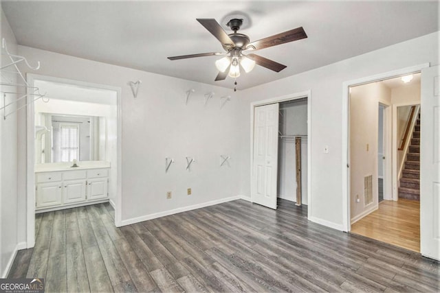 unfurnished bedroom featuring ceiling fan, ensuite bath, sink, a closet, and dark hardwood / wood-style flooring