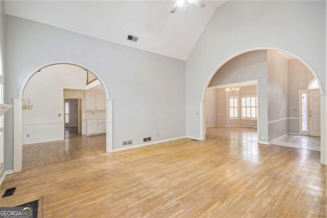 unfurnished room with high vaulted ceiling, light wood-type flooring, and ceiling fan with notable chandelier