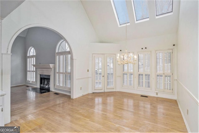 unfurnished living room with a skylight, a chandelier, light hardwood / wood-style floors, and high vaulted ceiling