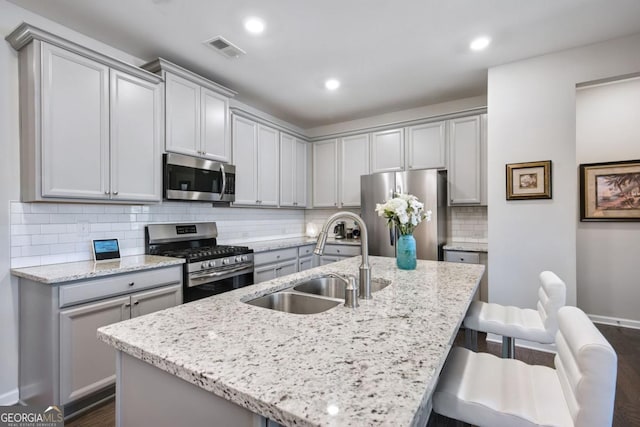 kitchen with light stone countertops, sink, a center island with sink, and stainless steel appliances