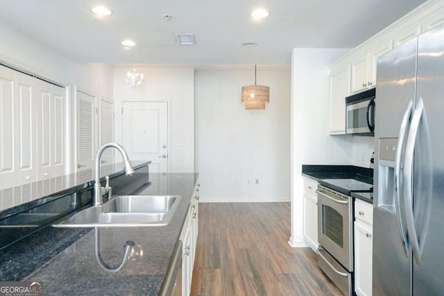 kitchen featuring appliances with stainless steel finishes, dark stone counters, pendant lighting, white cabinets, and sink