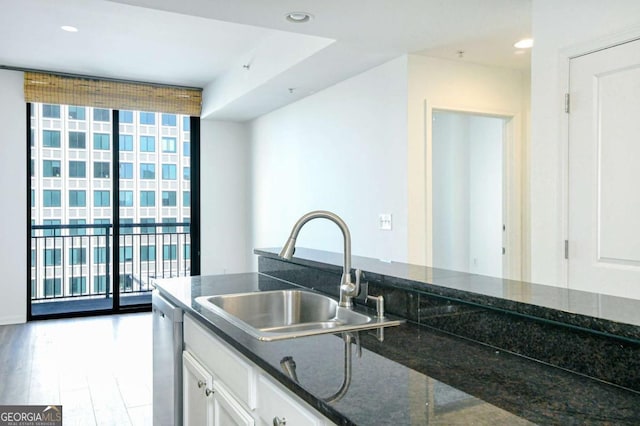 kitchen with white cabinetry, a wall of windows, dark stone countertops, sink, and stainless steel dishwasher