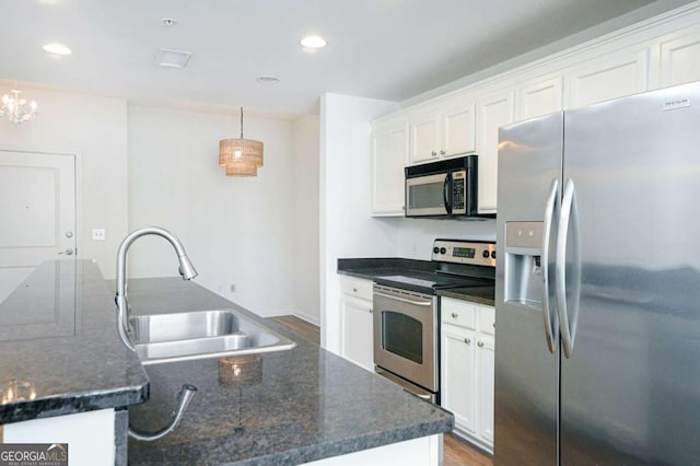 kitchen featuring white cabinets, appliances with stainless steel finishes, decorative light fixtures, dark stone counters, and sink