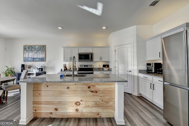 kitchen with sink, white cabinetry, stainless steel appliances, light stone countertops, and an island with sink