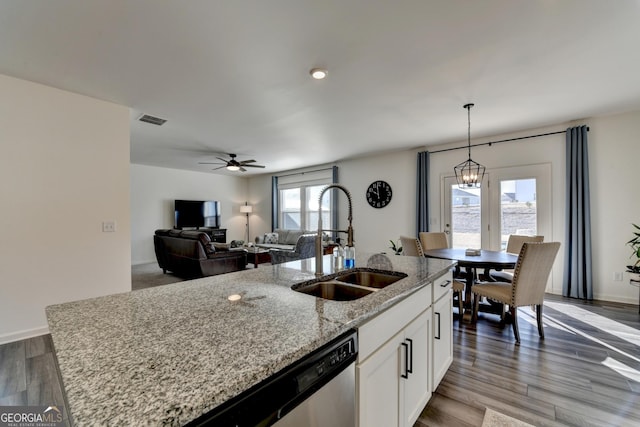 kitchen featuring pendant lighting, sink, light stone counters, an island with sink, and white cabinets