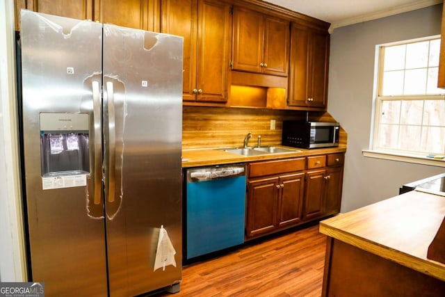 kitchen featuring stainless steel appliances, light hardwood / wood-style floors, sink, backsplash, and crown molding