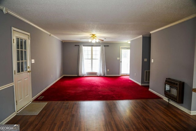 unfurnished living room featuring ceiling fan, heating unit, dark wood-type flooring, ornamental molding, and a textured ceiling