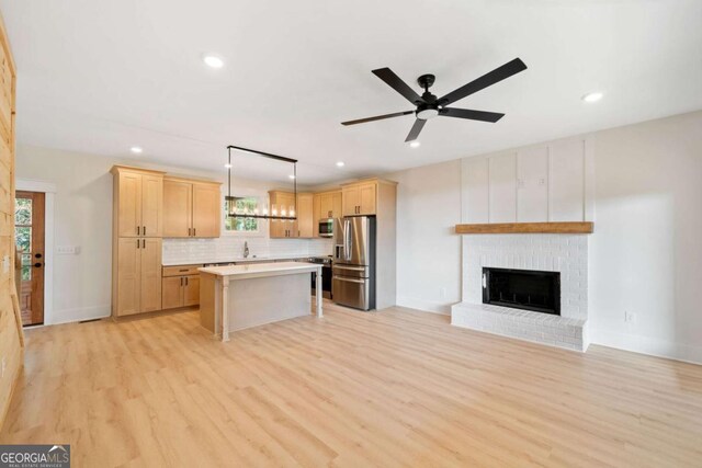 kitchen with ceiling fan, appliances with stainless steel finishes, light wood-type flooring, hanging light fixtures, and a kitchen island