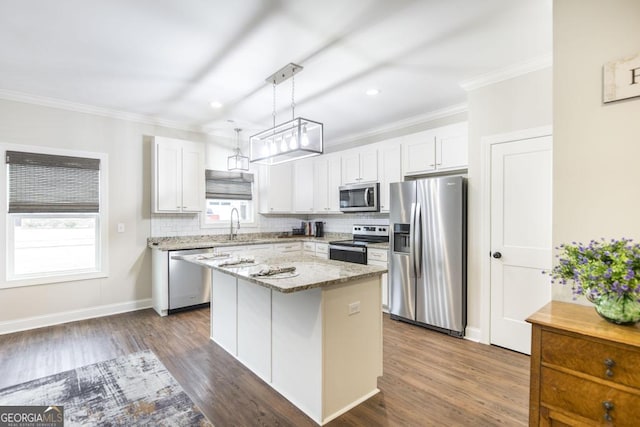 kitchen with appliances with stainless steel finishes, white cabinetry, a kitchen island, decorative light fixtures, and light stone counters