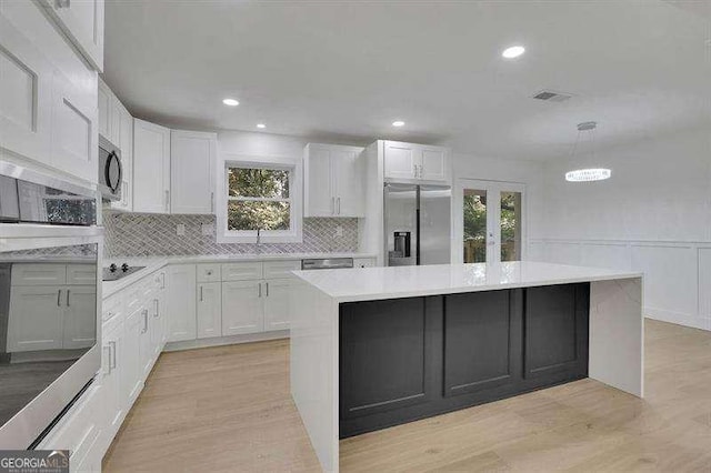 kitchen featuring appliances with stainless steel finishes, a center island, decorative light fixtures, white cabinetry, and backsplash