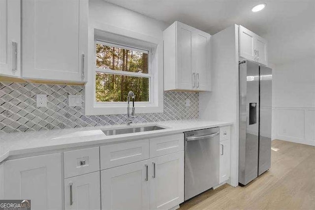 kitchen featuring decorative backsplash, sink, light wood-type flooring, appliances with stainless steel finishes, and white cabinets