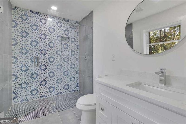 bathroom with toilet, vanity, tile patterned flooring, and tiled shower