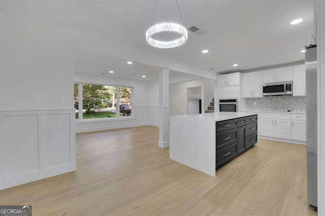 kitchen featuring decorative light fixtures, light hardwood / wood-style floors, decorative backsplash, stainless steel appliances, and white cabinets