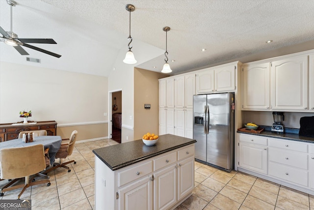 kitchen with stainless steel refrigerator with ice dispenser, vaulted ceiling, a textured ceiling, a kitchen island, and white cabinets