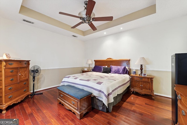 bedroom featuring ceiling fan, dark wood-type flooring, and a tray ceiling