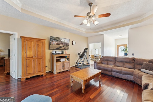 living room featuring a textured ceiling, dark wood-type flooring, ornamental molding, ceiling fan, and a tray ceiling