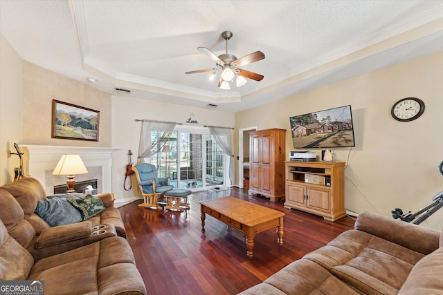 living room featuring ceiling fan, a tray ceiling, wood-type flooring, a textured ceiling, and crown molding