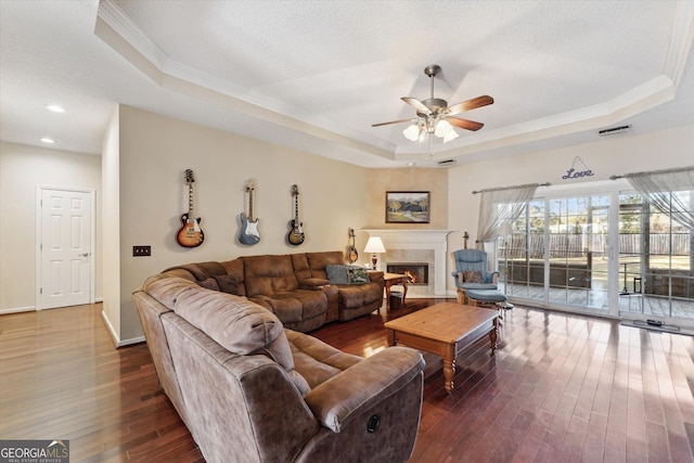 living room featuring ceiling fan, dark wood-type flooring, a tray ceiling, and crown molding