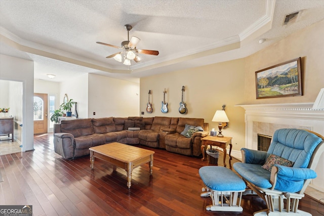 living room with a raised ceiling, dark wood-type flooring, a fireplace, a textured ceiling, and crown molding