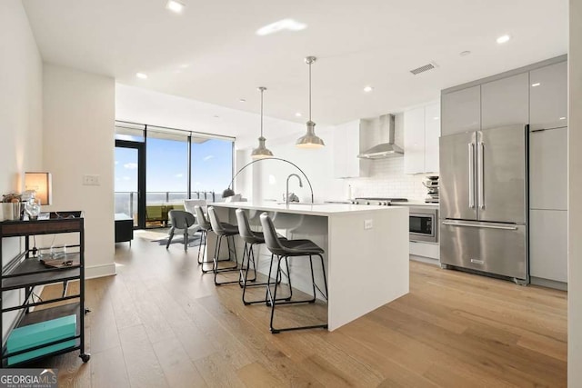 kitchen featuring pendant lighting, backsplash, light wood-type flooring, high end fridge, and wall chimney range hood