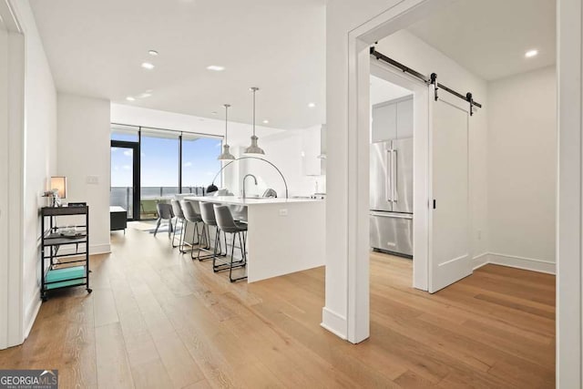 kitchen with light hardwood / wood-style floors, hanging light fixtures, a breakfast bar, high end refrigerator, and a barn door