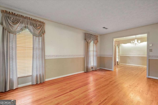 empty room featuring wood-type flooring, a notable chandelier, and a textured ceiling