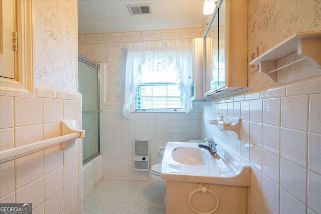 full bathroom featuring vanity, tile walls, toilet, combined bath / shower with glass door, and heating unit