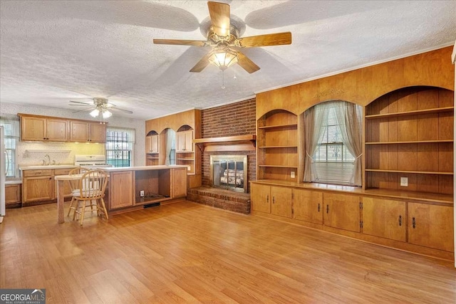 living room featuring built in features, light wood-type flooring, a brick fireplace, and a textured ceiling