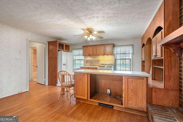 kitchen with white appliances, a textured ceiling, kitchen peninsula, ceiling fan, and light hardwood / wood-style flooring