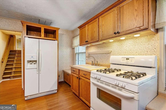 kitchen with sink, white appliances, a textured ceiling, and light wood-type flooring