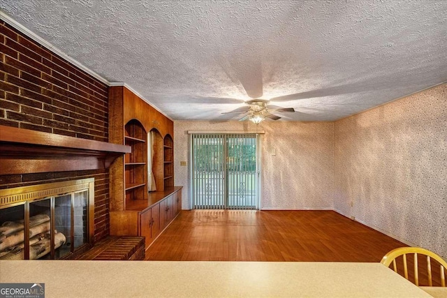 unfurnished living room with ceiling fan, a fireplace, wood-type flooring, ornamental molding, and built in shelves