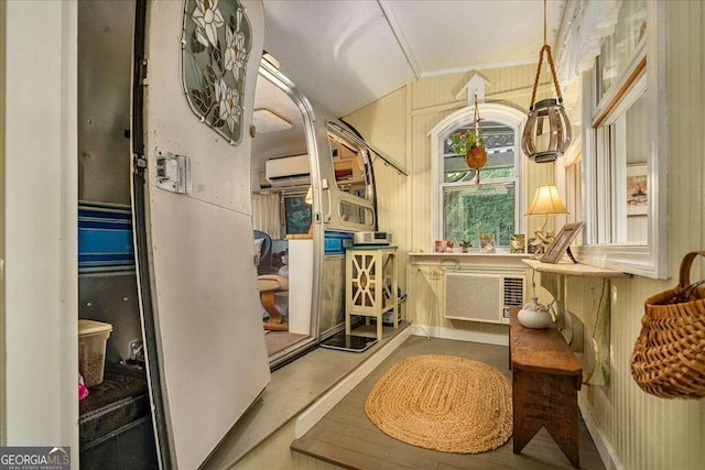 corridor with vaulted ceiling, a wall unit AC, and wood walls