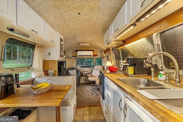 kitchen with white cabinets, wood counters, vaulted ceiling, light tile patterned floors, and stove