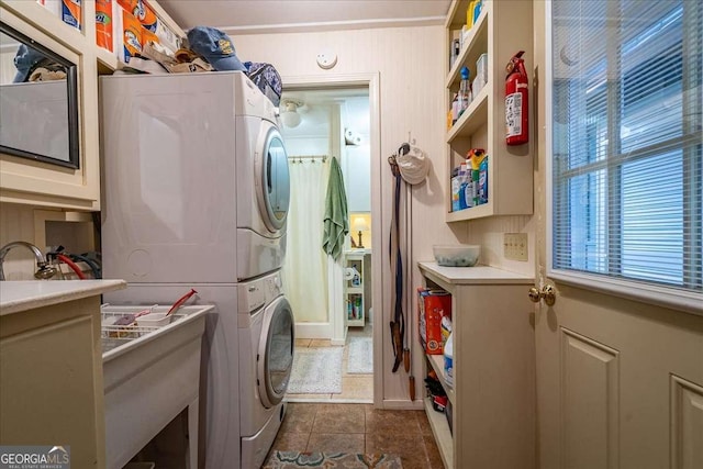 laundry area with stacked washer and clothes dryer and dark tile patterned flooring