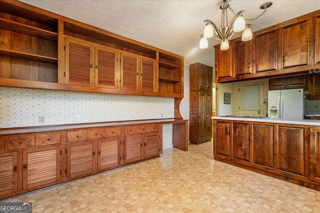 kitchen featuring stainless steel gas stovetop, hanging light fixtures, white refrigerator with ice dispenser, a textured ceiling, and a chandelier