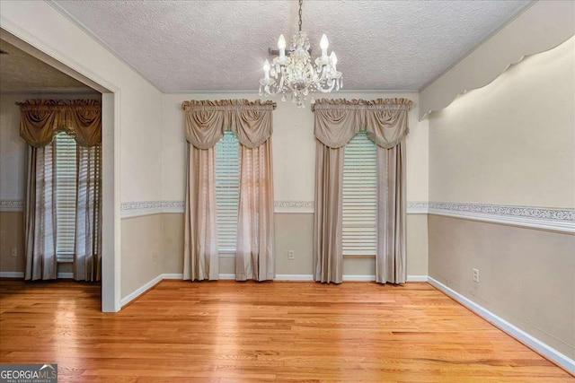 unfurnished dining area with light hardwood / wood-style floors, a textured ceiling, crown molding, and a chandelier