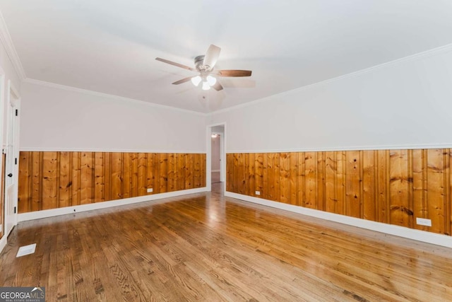 spare room with ceiling fan, wood walls, crown molding, and hardwood / wood-style flooring