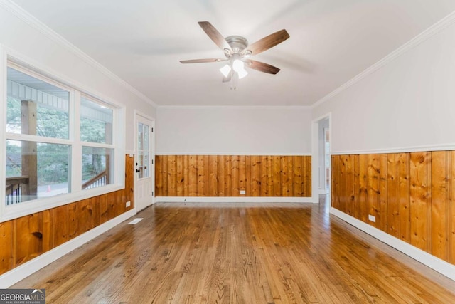 unfurnished room with ceiling fan, wood-type flooring, wood walls, and ornamental molding