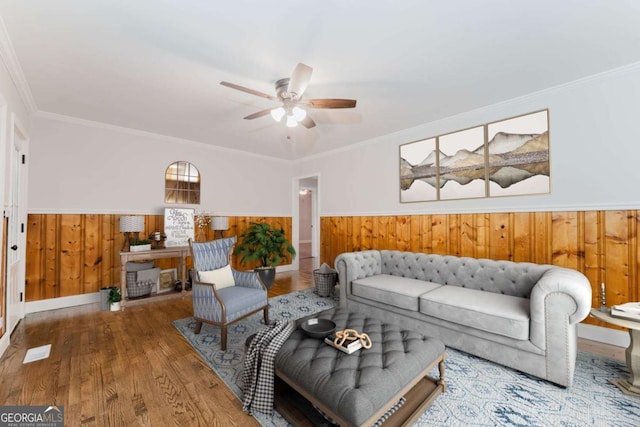 living room with ceiling fan, hardwood / wood-style floors, ornamental molding, and wooden walls