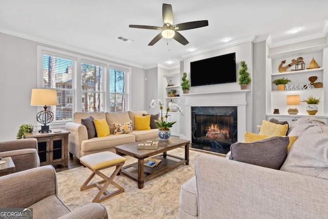 living room with a premium fireplace, ornamental molding, built in features, and ceiling fan