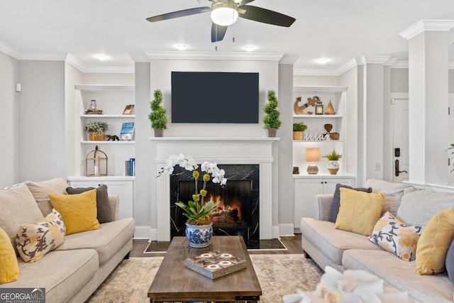 living room featuring hardwood / wood-style floors, ceiling fan, a premium fireplace, ornamental molding, and built in shelves