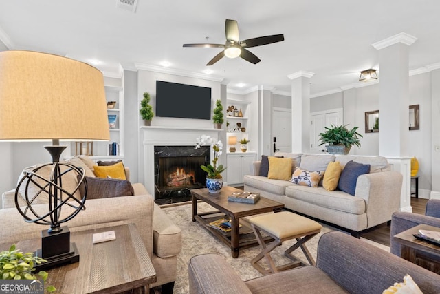 living room with ceiling fan, wood-type flooring, a high end fireplace, crown molding, and built in shelves