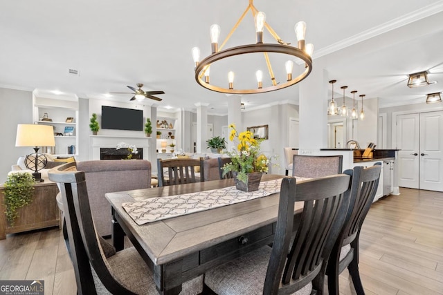 dining space with built in shelves, ceiling fan with notable chandelier, ornamental molding, and light hardwood / wood-style floors